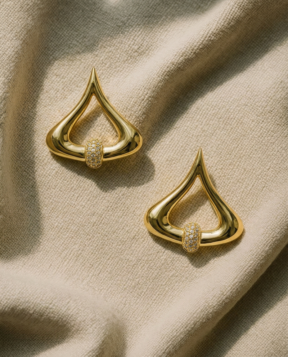Pair of gold statement earrings in an open drop shape with a cut crystal pavé rondelle at the base.