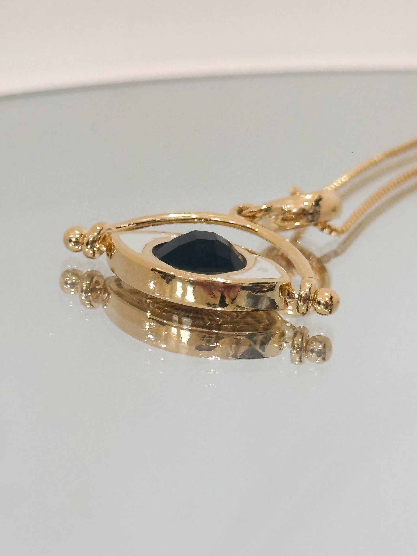 Gold necklace with a dark stone pendant on a light gray background