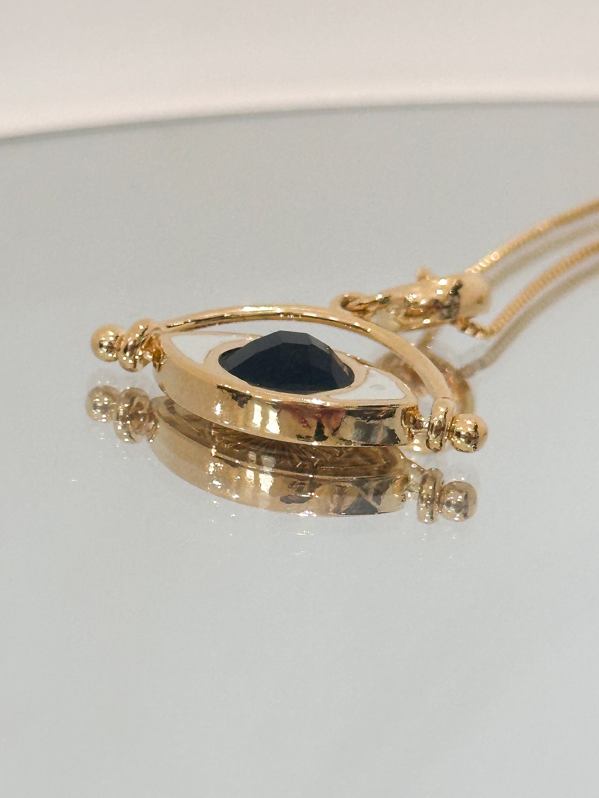 Gold necklace with a dark stone pendant on a light gray background