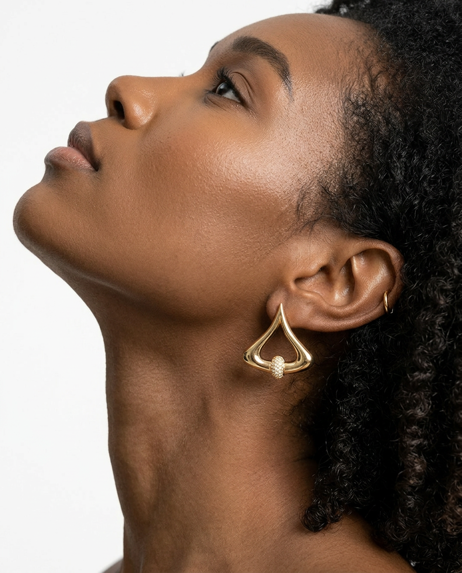 Gold statement earrings with a cut crystal pavé detail, worn by a woman shown in profile with her head tilted upward.