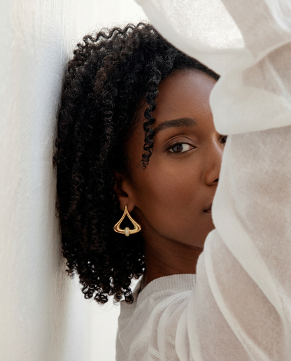 Gold statement earrings with a cut crystal pavé detail, worn by a woman