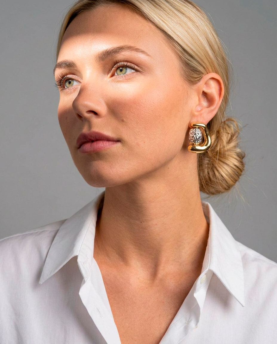Woman wearing two-tone statement earrings with a rounded gold finish and textured silver-tone center.