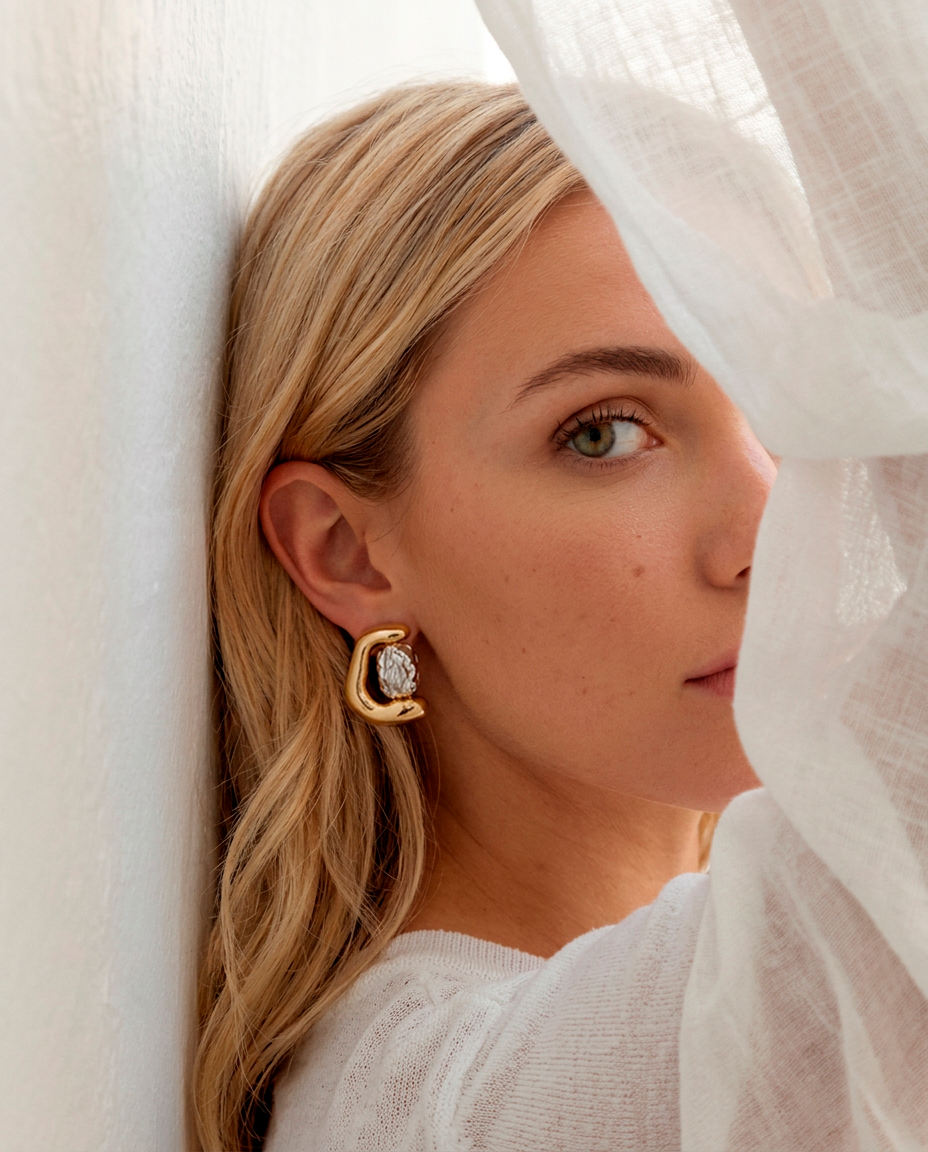 Woman wearing two-tone statement earrings with a rounded gold finish and textured silver-tone center.